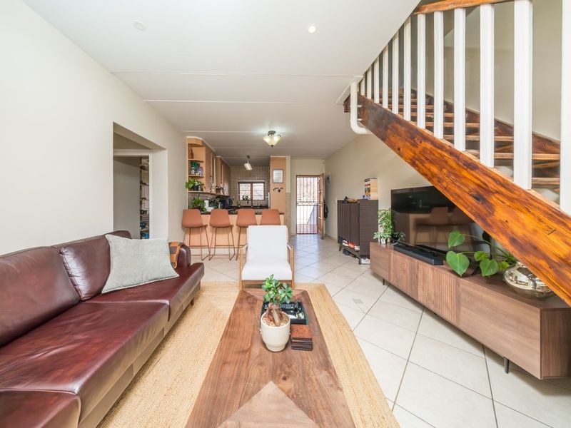 Open-plan living area featuring tiled floors, a wooden staircase, and a functional kitchen with a breakfast bar, leading to an exterior security gate.