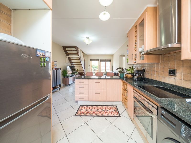 Open-plan kitchen featuring light wood cabinetry, granite countertops, and integrated appliances, flowing into the living area with a staircase leading to the upper level.