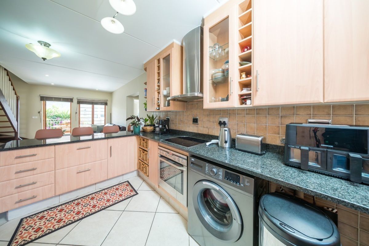 A functional kitchen featuring light wood cabinetry, granite countertops, integrated appliances, and a breakfast bar, seamlessly flowing into the adjacent living area.