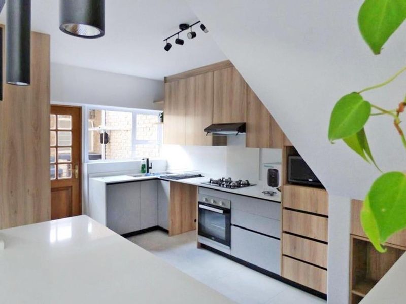 Modern kitchen featuring light wood-tone cabinetry, stone countertops, integrated gas hob, electric oven, and efficient under-stair storage design.