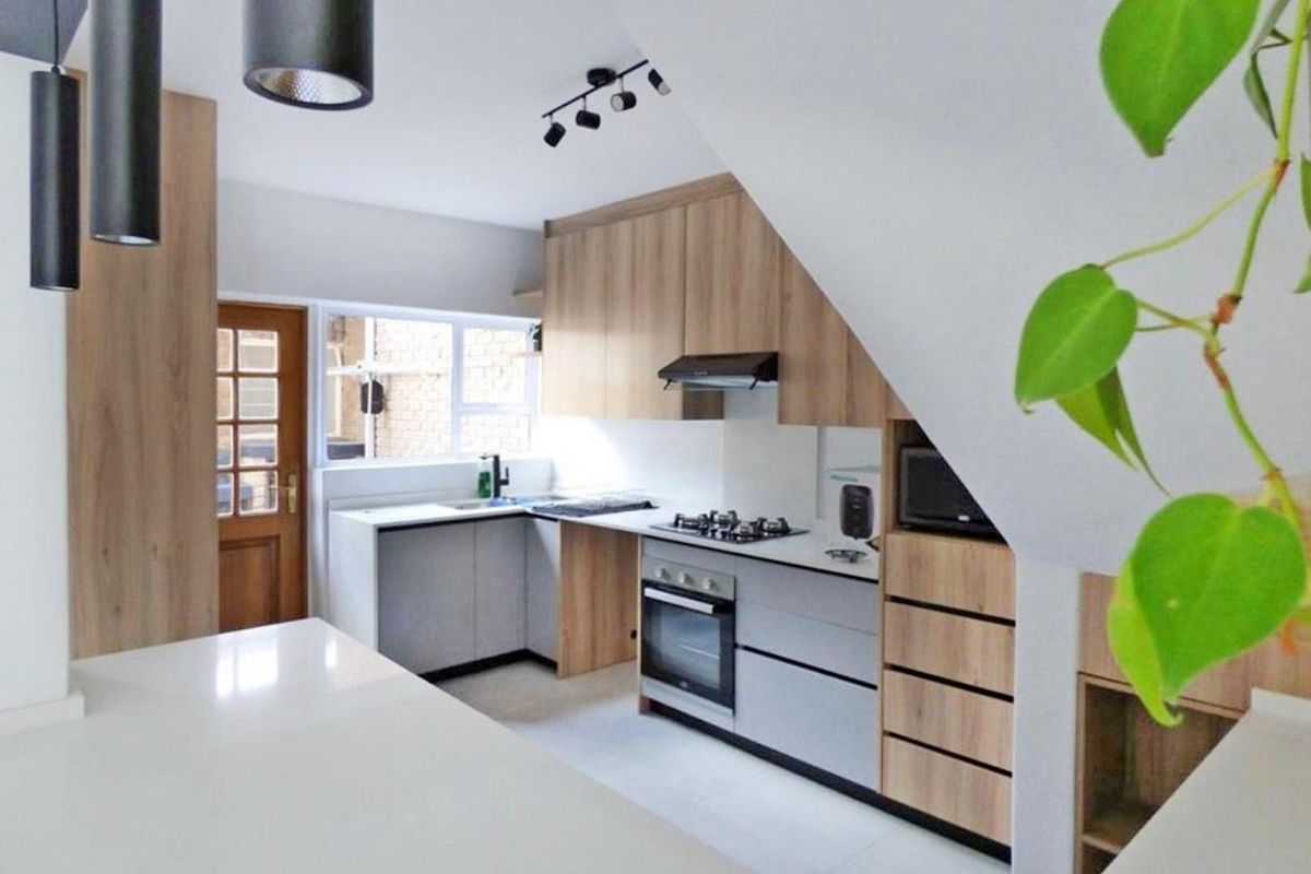 Modern kitchen featuring light wood-tone cabinetry, stone countertops, integrated gas hob, electric oven, and efficient under-stair storage design.