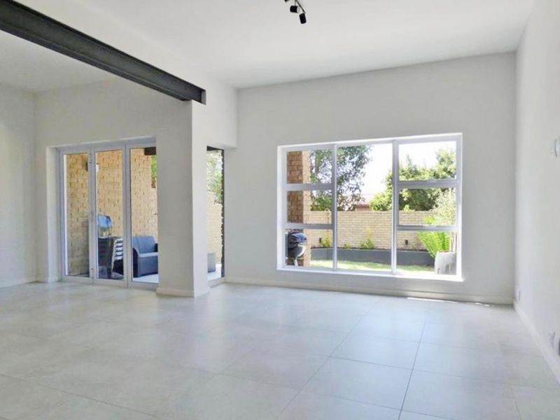 Spacious, light-filled living area featuring modern tiled flooring, an exposed steel beam, and large windows providing views of the rear garden and patio.