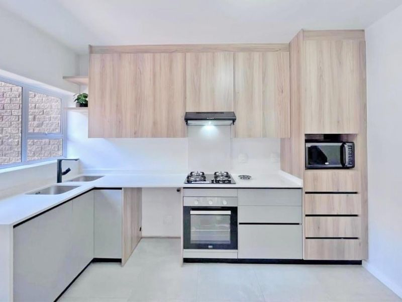 Modern kitchen featuring light wood-grain cabinetry, stone countertops, integrated gas hob, oven, and built-in microwave with clean, contemporary finishes.