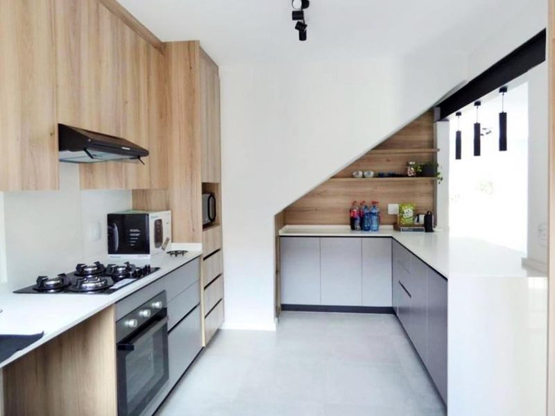 Modern kitchen featuring light wood and grey cabinetry, stone countertops, gas hob, built-in oven, and efficient under-stair storage integration.