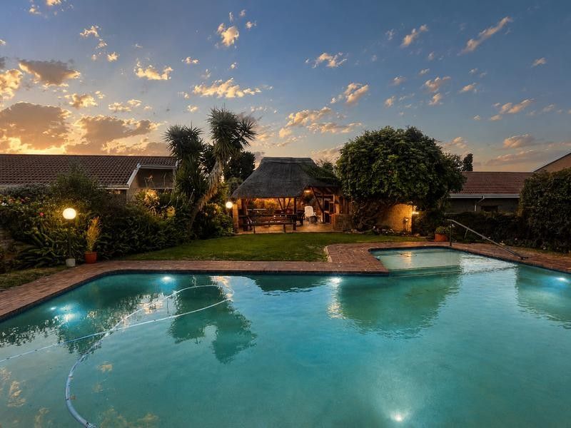 A well-maintained outdoor pool area featuring a swimming pool, brick paving, and a traditional thatched lapa, perfect for outdoor entertaining.
