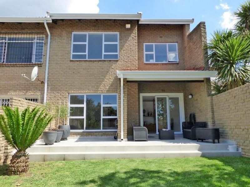 Rear view of a two-story brick townhouse featuring a paved patio area, sliding glass doors, and a private garden space.
