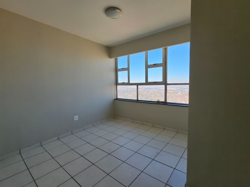An empty bedroom featuring tiled flooring, neutral walls, and large windows offering expansive city views.