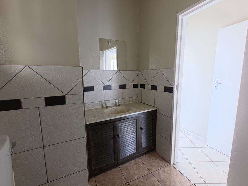A functional bathroom featuring a vanity cabinet with basin, tiled splashback, and wall mirror, requiring cosmetic updates to improve its overall condition.