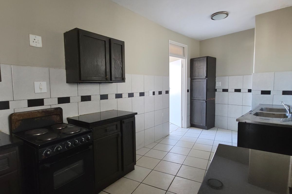 A functional kitchen featuring dark cabinetry, granite countertops, a built-in electric stove, and a double sink with tiled backsplash and flooring.