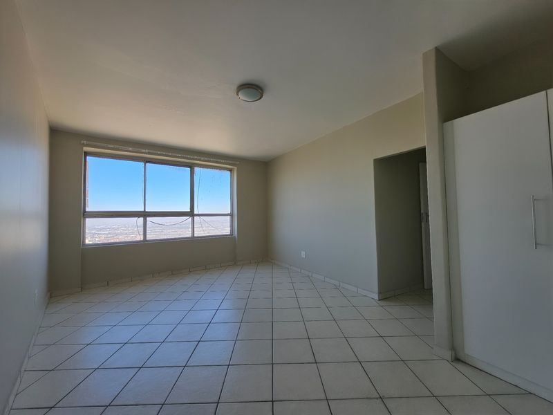 An empty bedroom featuring tiled flooring, a built-in wardrobe, and a large window with expansive city views.