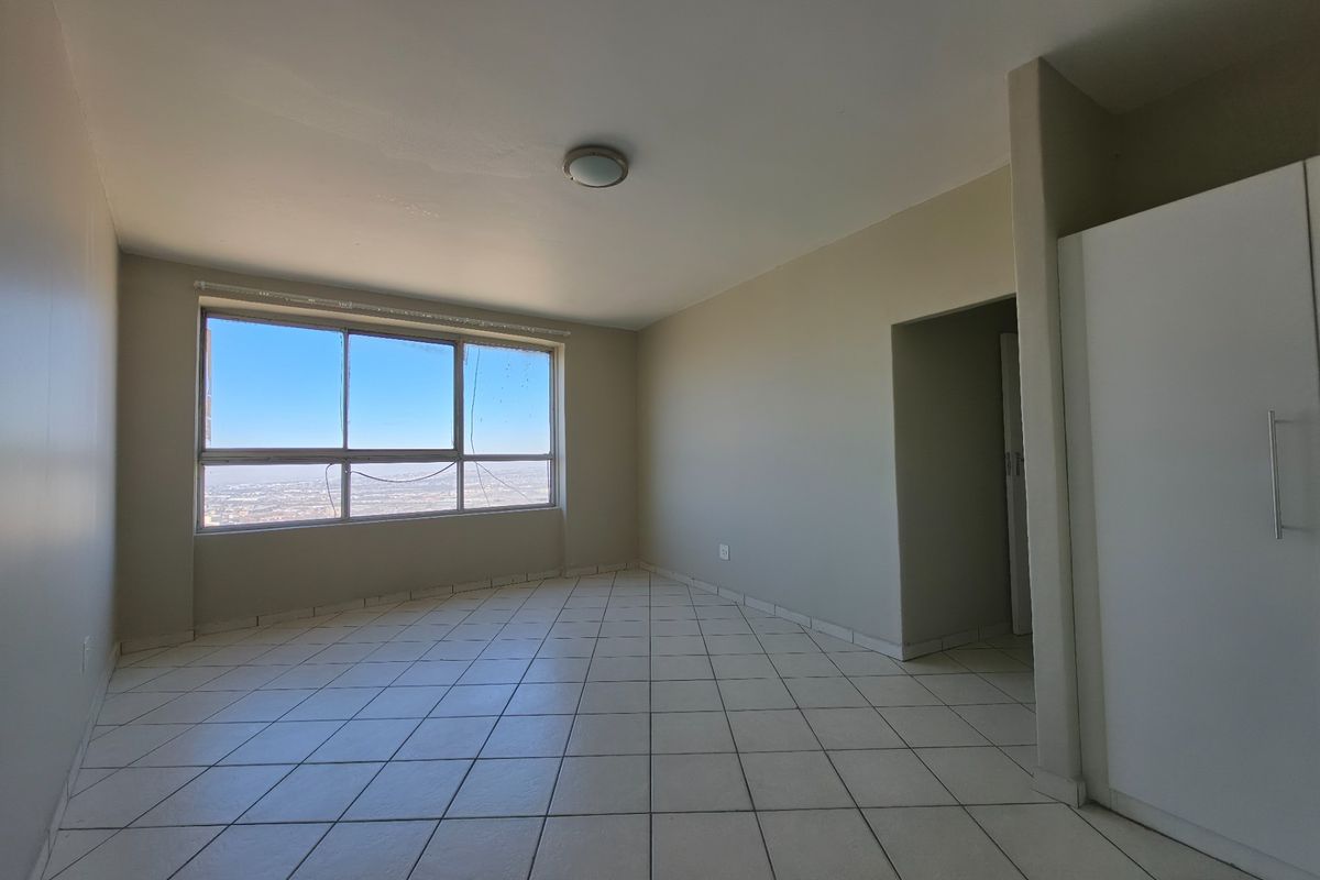 An empty bedroom featuring tiled flooring, a built-in wardrobe, and a large window with expansive city views.