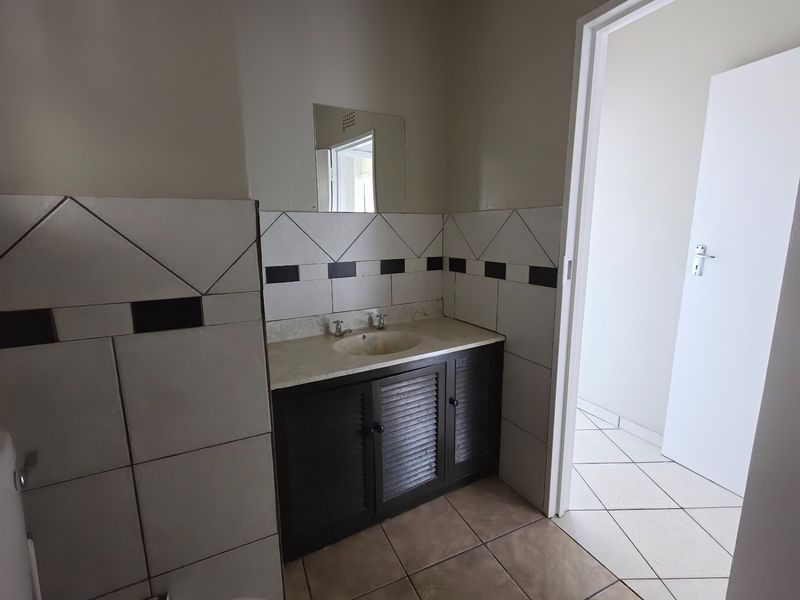 A functional bathroom featuring a vanity cabinet with a basin, wall mirror, and tiled splashback, presenting an opportunity for modern cosmetic updates.
