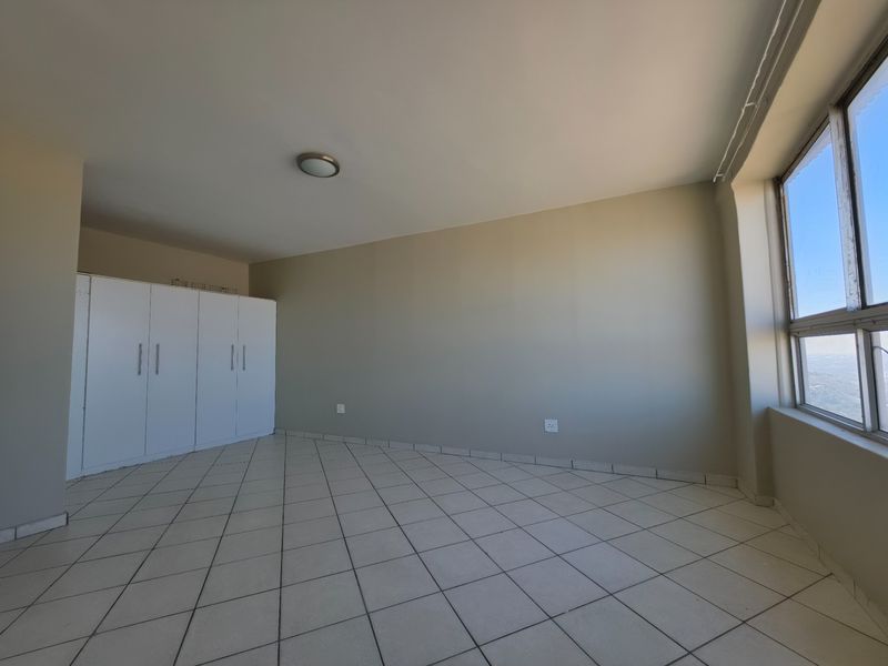 A bright, empty bedroom featuring neutral walls, tiled flooring, and built-in cupboards, offering a clean canvas for personalization.