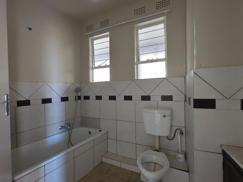 A dated bathroom featuring a built-in bathtub, toilet, and tiled finishes. The space is vacant and ready for modernization.