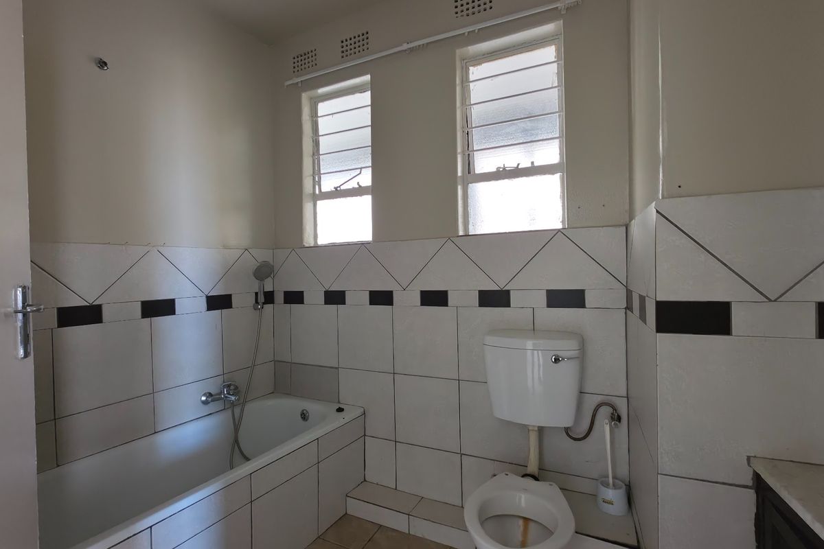 A dated bathroom featuring a built-in bathtub, toilet, and tiled finishes. The space is vacant and ready for modernization.