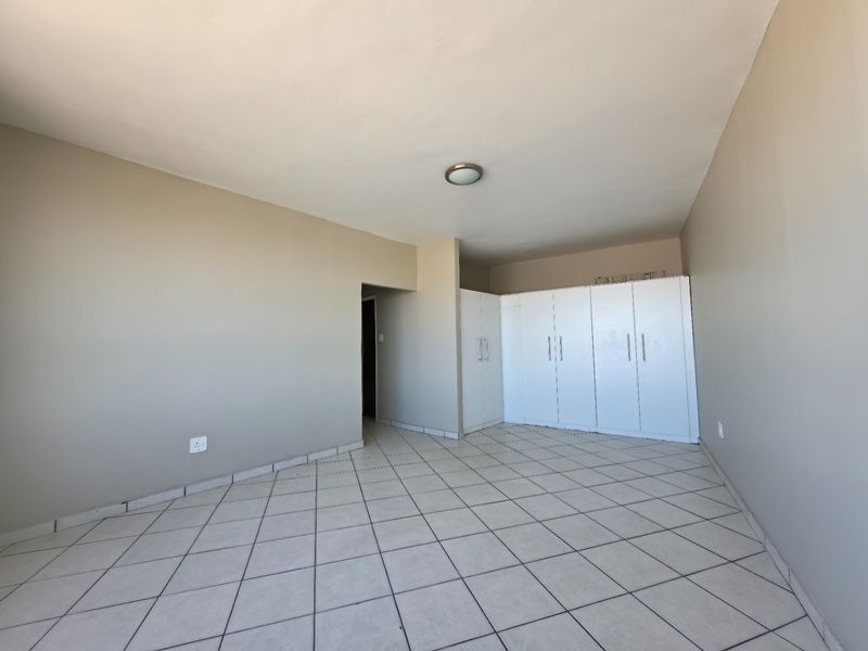 A spacious, empty bedroom featuring neutral wall tones, tiled flooring, and ample built-in cupboard storage.