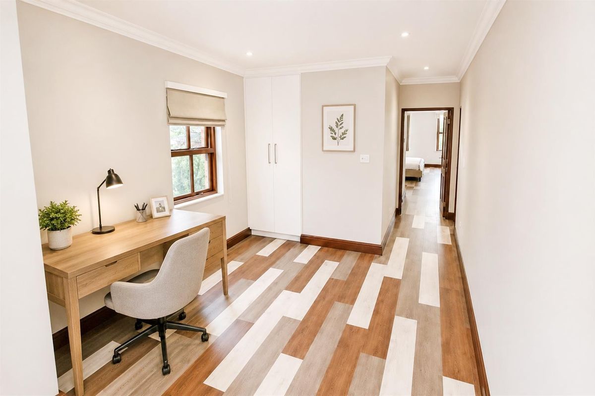 A well-lit bedroom featuring modern timber-look flooring, built-in wardrobe storage, and recessed downlighting, with a view through to an adjoining room.
