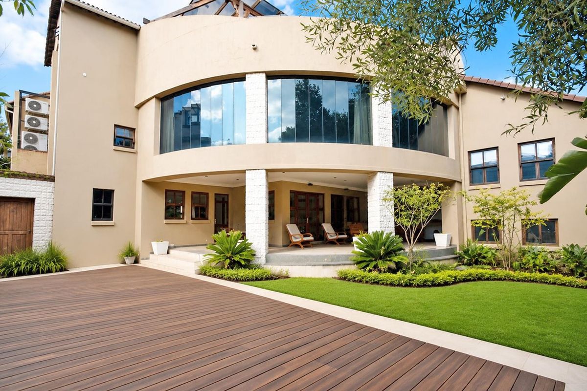 A well-maintained rear exterior featuring a spacious timber deck, landscaped garden, and a striking curved architectural facade with a covered patio area.