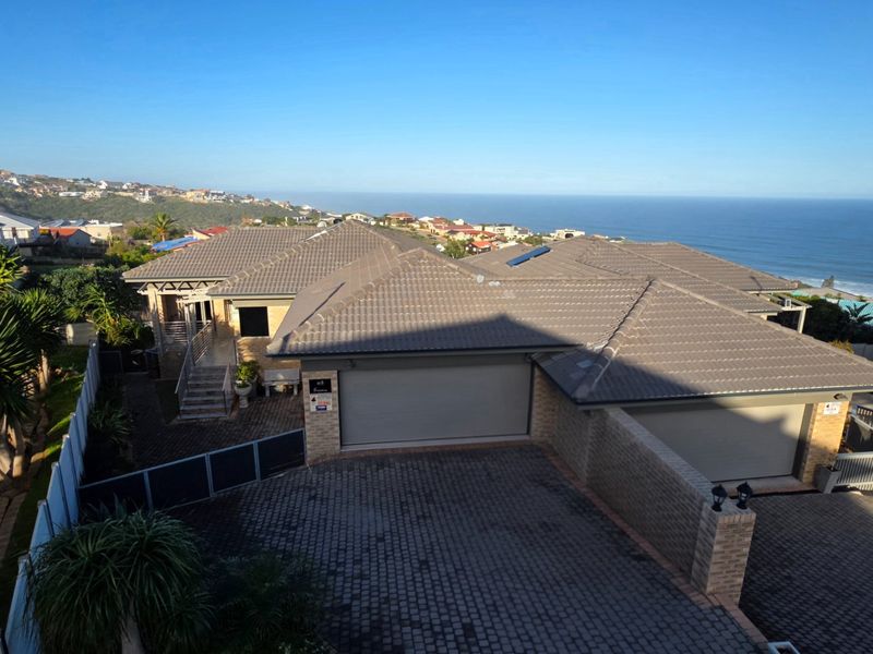 Aerial view of a residential property featuring a tiled roof, double garage, paved driveway, and ocean views in the background.