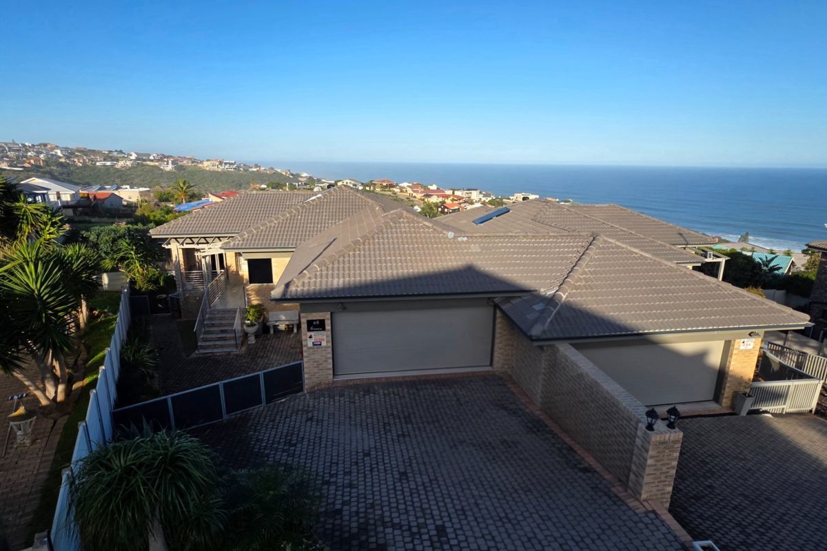 Aerial view of a residential property featuring a tiled roof, double garage, paved driveway, and ocean views in the background.