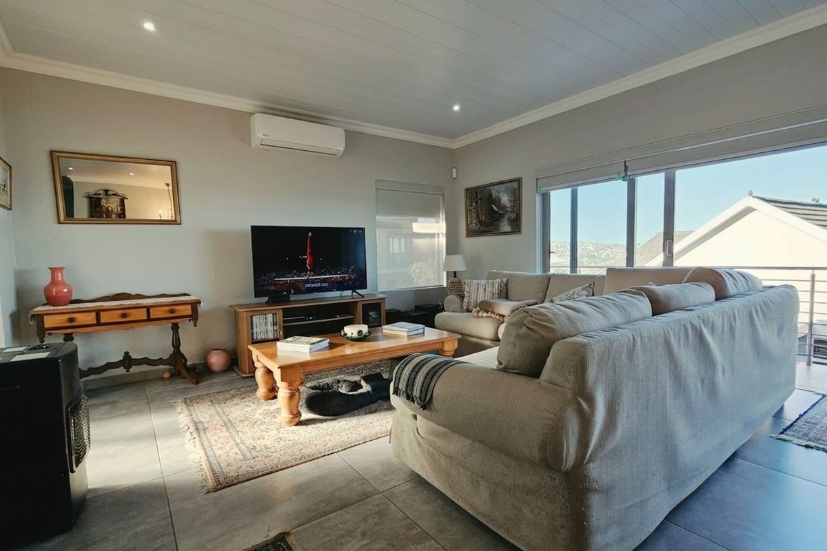 A bright and spacious living room featuring tiled floors, a split-system air conditioner, and large sliding glass doors that open to an outdoor area.