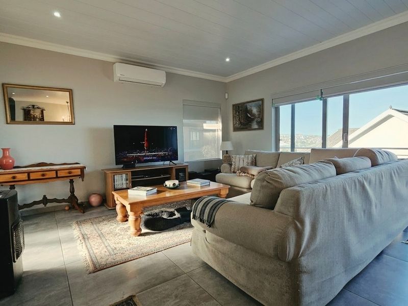 A bright and spacious living room featuring tiled floors, a split-system air conditioner, and large sliding glass doors that open to an outdoor area.