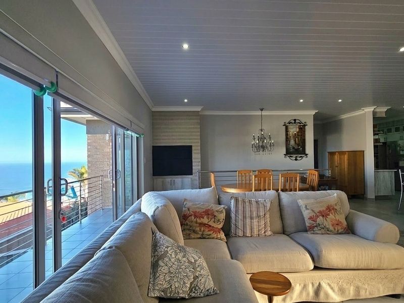 Spacious open-plan living and dining area featuring a modern kitchen, recessed lighting, and large sliding doors opening onto a balcony with ocean views.