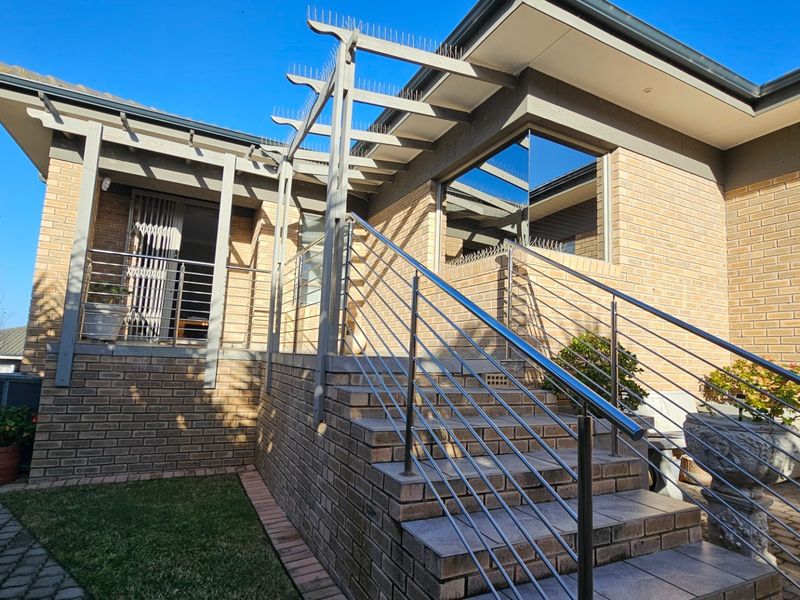 A well-maintained outdoor patio area featuring a brick staircase with stainless steel balustrades and a pergola structure with integrated bird deterrent spikes.