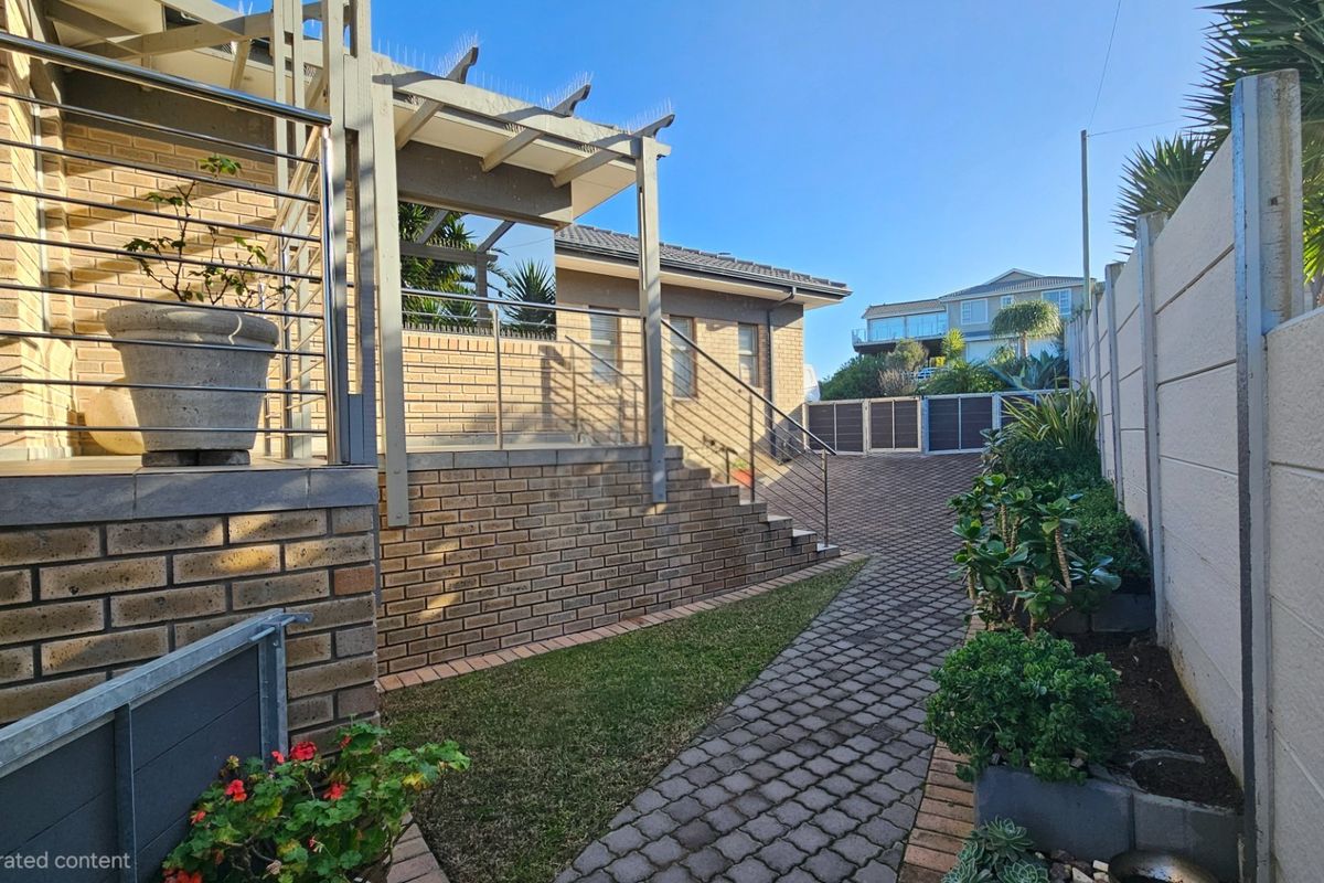 A well-maintained rear exterior area featuring a brick facade, paved driveway, and a pergola structure with stairs leading to the main dwelling.