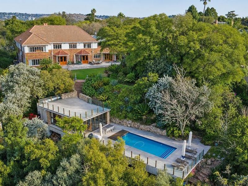 Aerial view of a large multi-level residential property featuring a swimming pool, expansive landscaped gardens, and a classic brick home with a tiled roof.