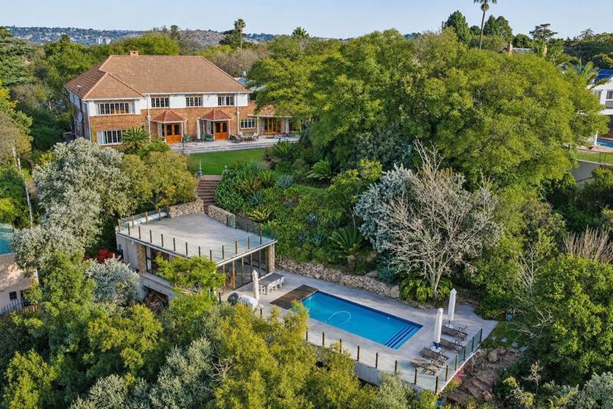 Aerial view of a large multi-level residential property featuring a swimming pool, expansive landscaped gardens, and a classic brick home with a tiled roof.