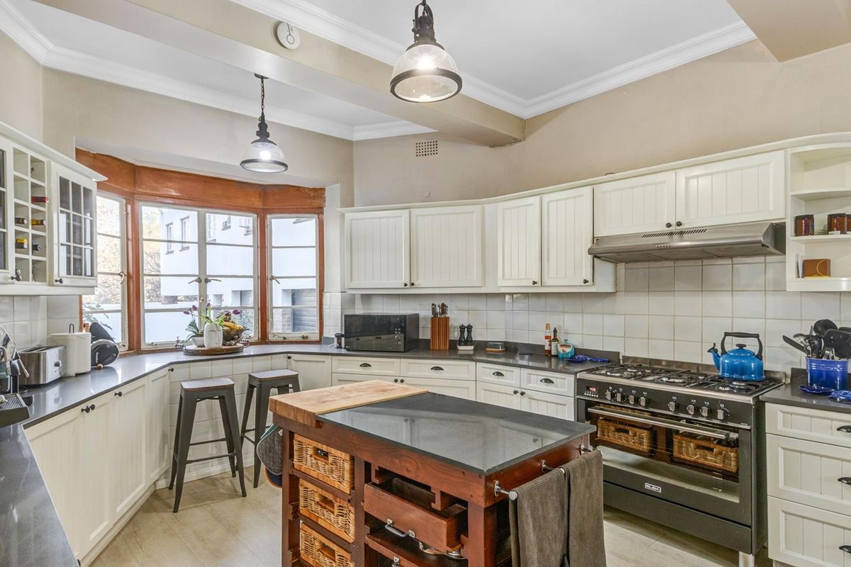 A well-appointed kitchen featuring white cabinetry, dark stone countertops, a gas stove with extractor fan, and a charming bay window with breakfast seating.