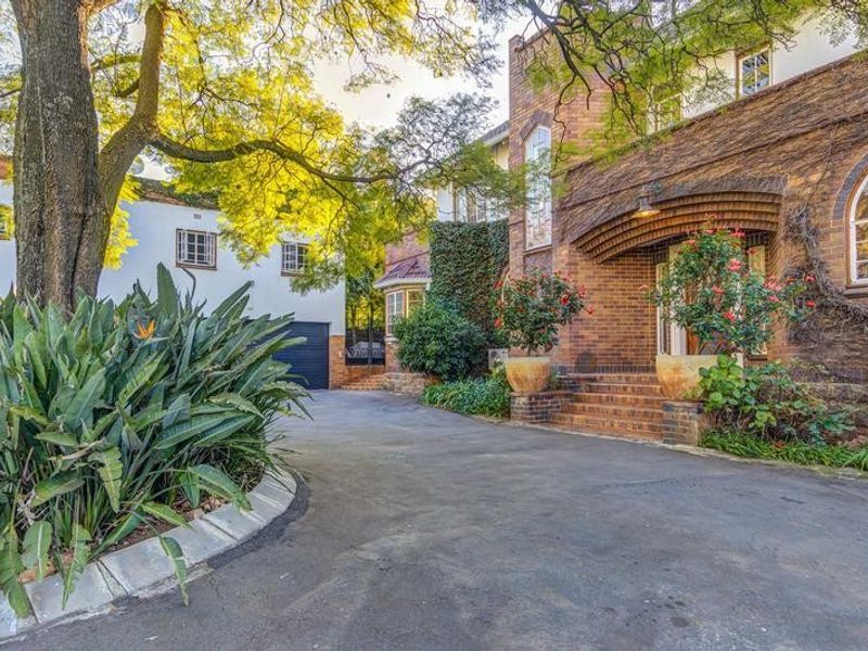 A charming front exterior view featuring a brick facade, arched windows, a covered entrance with brick steps, and a paved driveway.