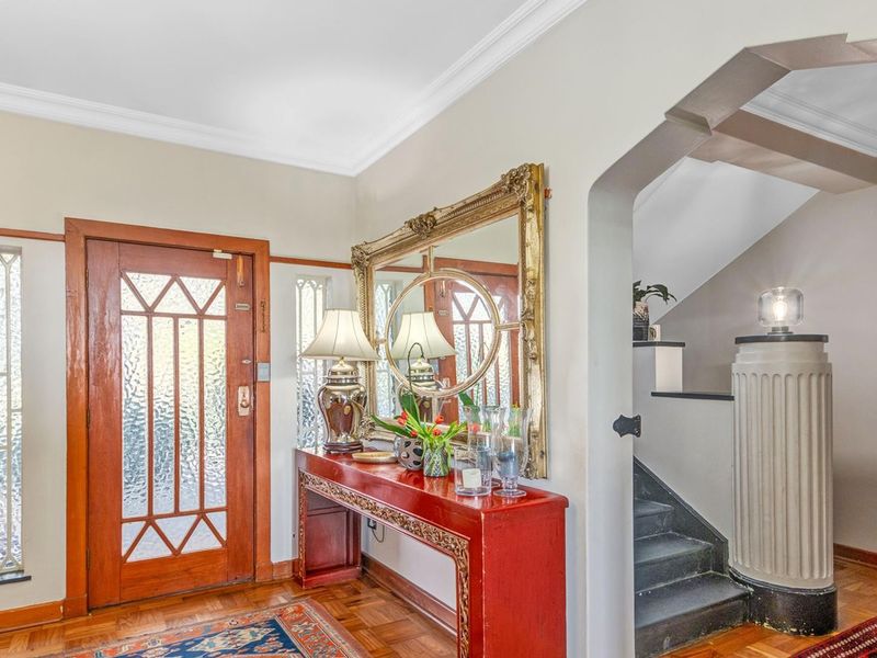 Welcoming entrance hall featuring classic timber front door with leaded glass sidelights, elegant parquet flooring, and a distinctive architectural archway leading to the staircase.