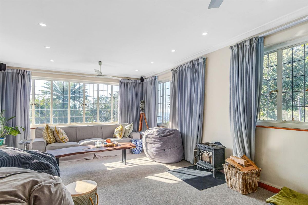 A bright and spacious living room featuring large multi-pane windows, recessed lighting, a ceiling fan, and a cozy freestanding wood-burning stove on a hearth.