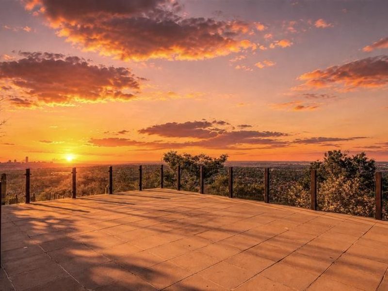 An expansive elevated terrace featuring a glass balustrade, offering panoramic sunset views over the surrounding landscape and city skyline.
