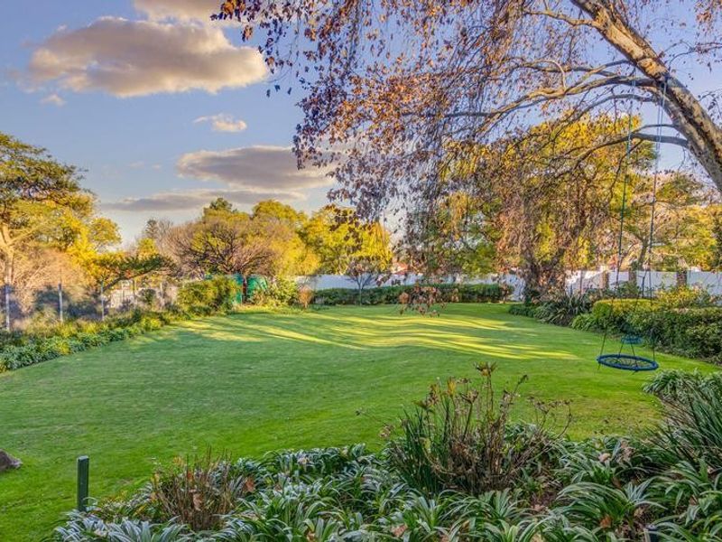 A spacious, well-maintained private garden featuring a large manicured lawn, mature trees, and perimeter fencing.