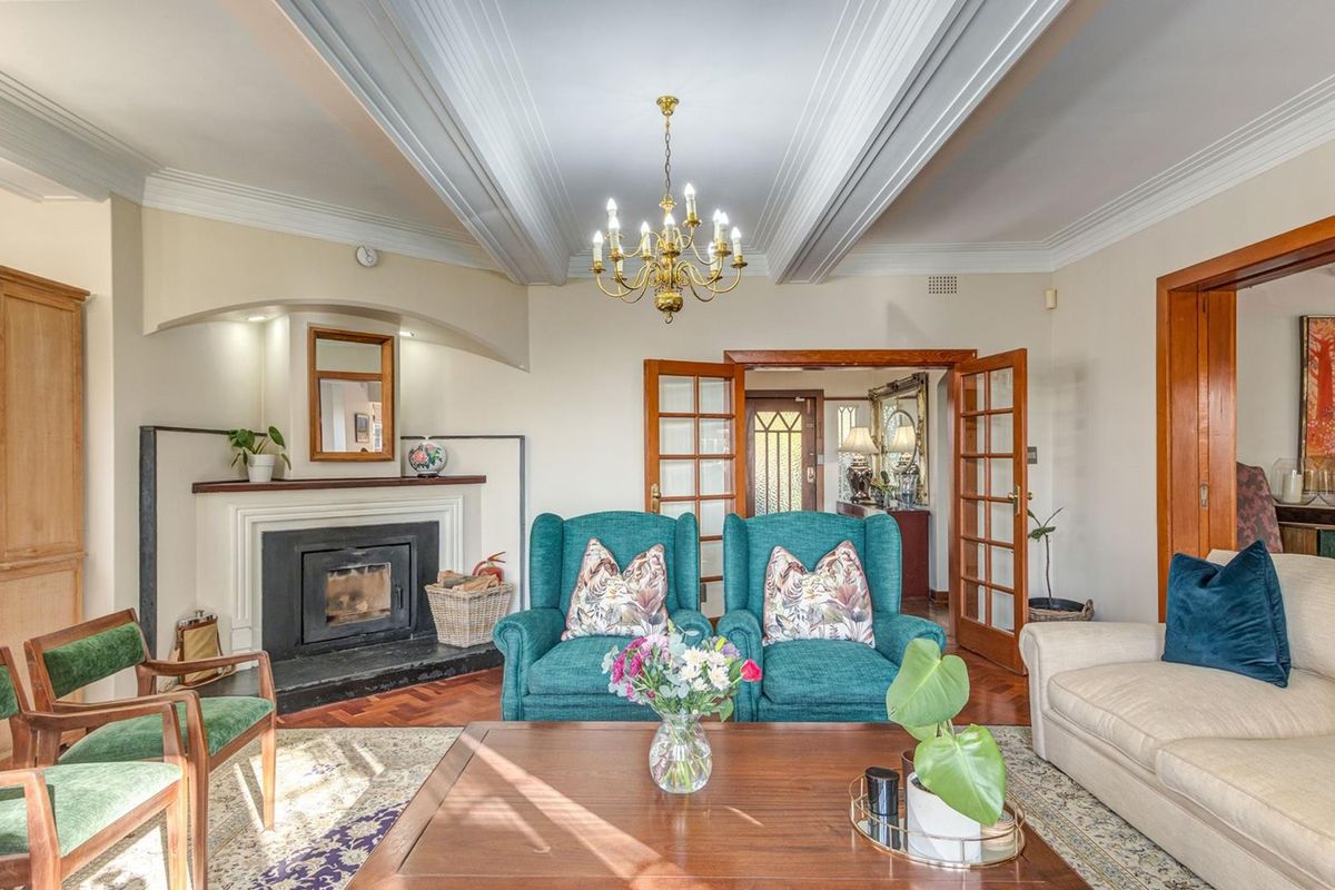 Elegant living room featuring a classic fireplace, intricate coffered ceilings, warm parquet flooring, and traditional French doors leading to the entrance hall.