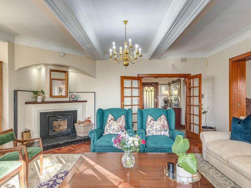 Elegant living room featuring a classic fireplace, intricate coffered ceilings, warm parquet flooring, and traditional French doors leading to the entrance hall.
