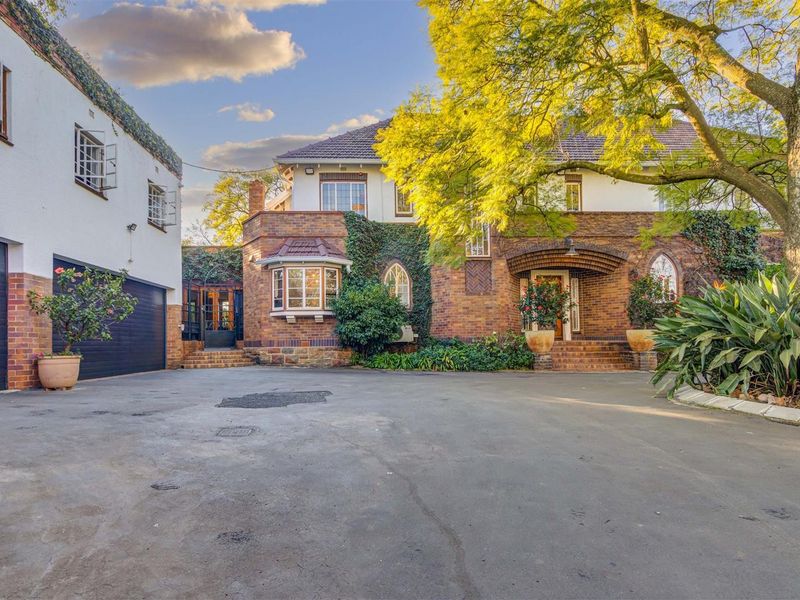 A charming character home featuring a classic brick facade, arched entrance, bay window, and a spacious asphalt driveway with an attached double garage.