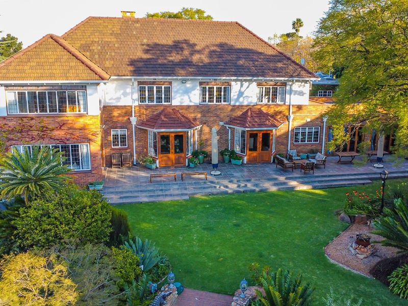 Aerial view of the rear elevation featuring a spacious tiled patio, established garden, and classic brick architecture with timber french doors.