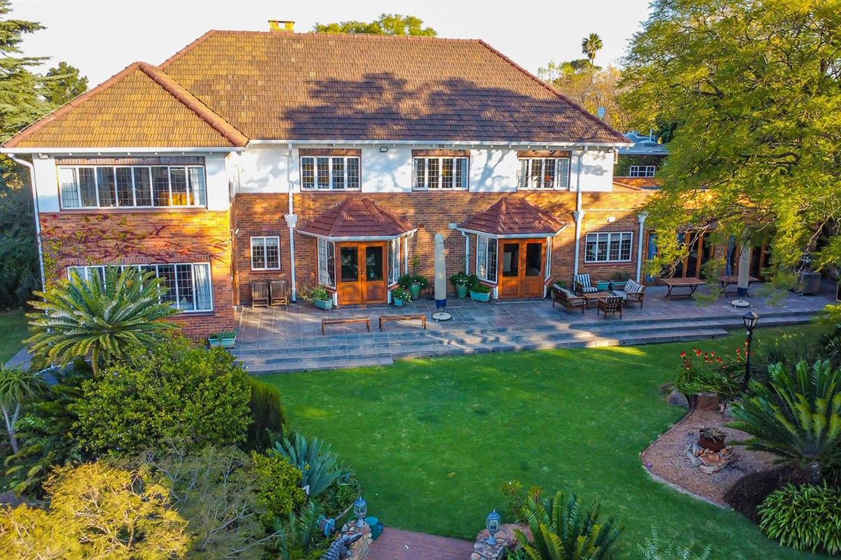 Aerial view of the rear elevation featuring a spacious tiled patio, established garden, and classic brick architecture with timber french doors.