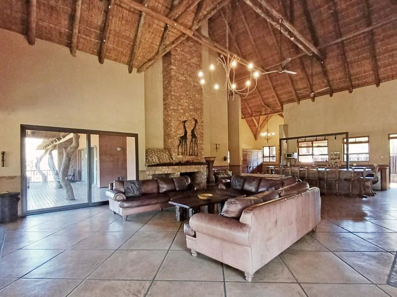 Spacious open-plan living area featuring a high thatched ceiling with exposed timber trusses, a large brick fireplace, and an integrated bar area.