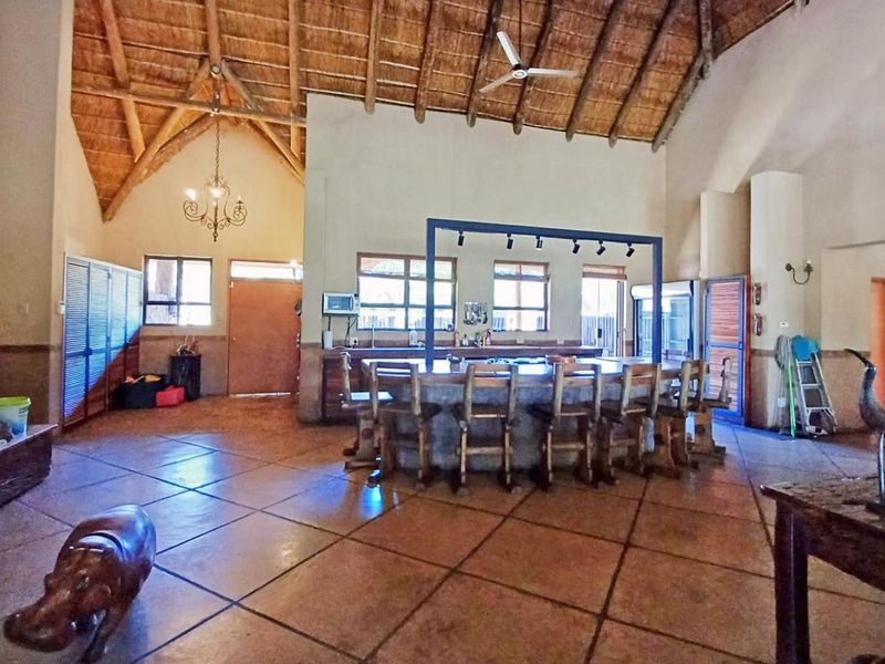 Spacious open-plan living area featuring a high thatched ceiling with exposed timber trusses, tiled flooring, and a large built-in bar counter.