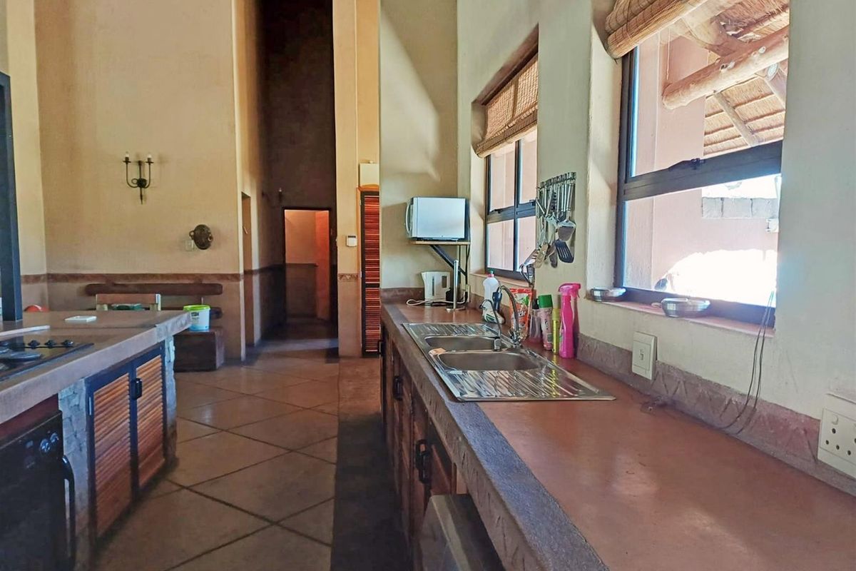 A rustic-style kitchen featuring built-in cabinetry, stone-look countertops, a double bowl stainless steel sink, and tiled flooring with high ceilings.