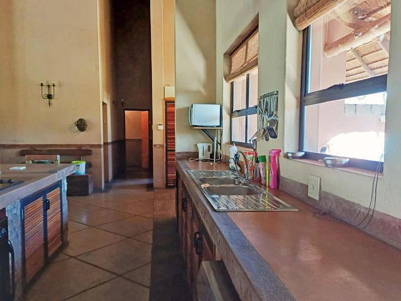A rustic-style kitchen featuring built-in cabinetry, stone-look countertops, a double bowl stainless steel sink, and tiled flooring with high ceilings.