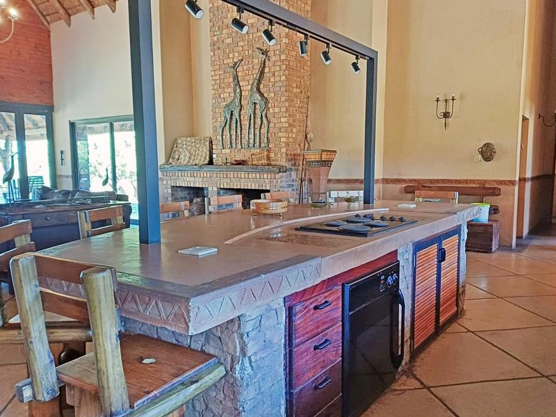 Spacious open-plan living area featuring a large kitchen island with built-in appliances, a prominent brick fireplace, and high ceilings with exposed timber rafters.