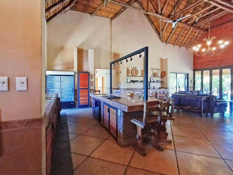 Spacious open-plan living area featuring a high thatched ceiling with exposed trusses, a central kitchen island, and tiled flooring throughout.