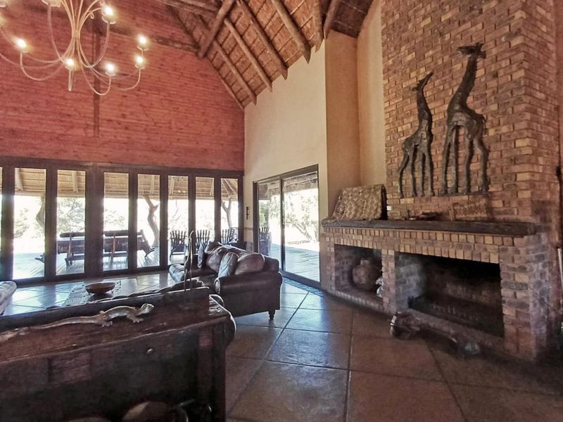 Spacious living room featuring a high exposed thatch ceiling, large brick fireplace, tiled floors, and expansive glass doors opening to an outdoor patio area.