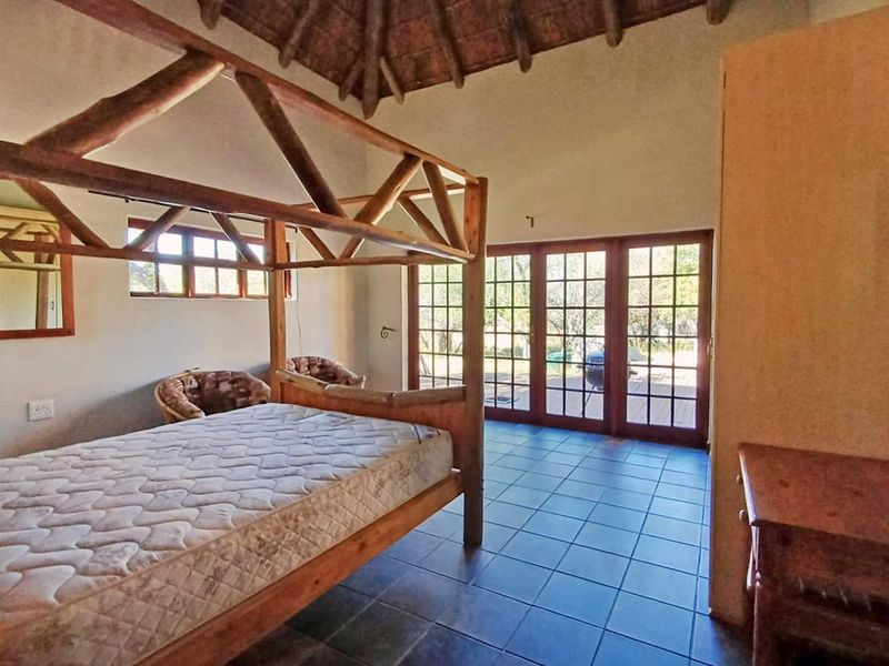 Spacious bedroom featuring a high thatched ceiling with exposed rafters, tiled flooring, and direct access to the outdoors through glass-paned french doors.